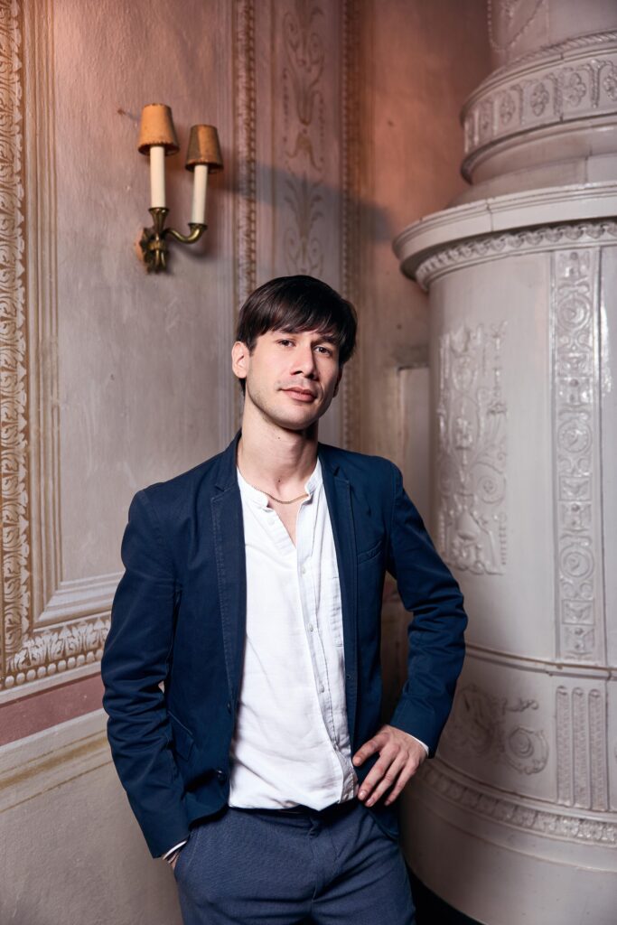 A formal portrait of composer and conductor Theo Thorsson taken by Valerie-Marie Voithofer in June 2025. The photograph was shot in a historic interior setting in Schloß Karlslust