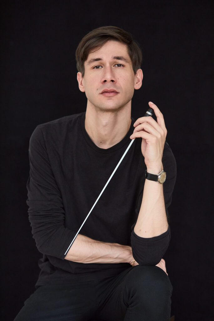 Portrait of composer and conductor Theo Thorsson holding a baton against a dark background.