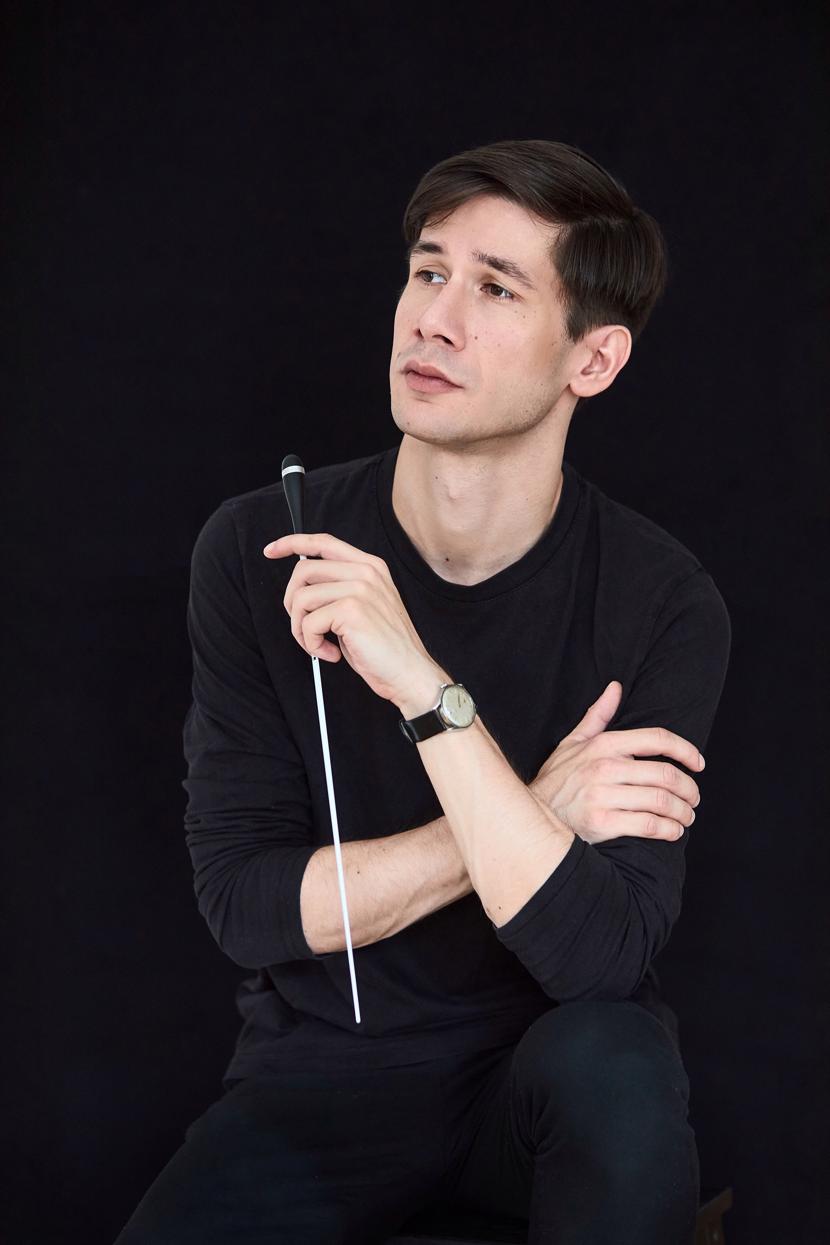 Portrait of composer and conductor Theo Thorsson holding a baton against a black background.